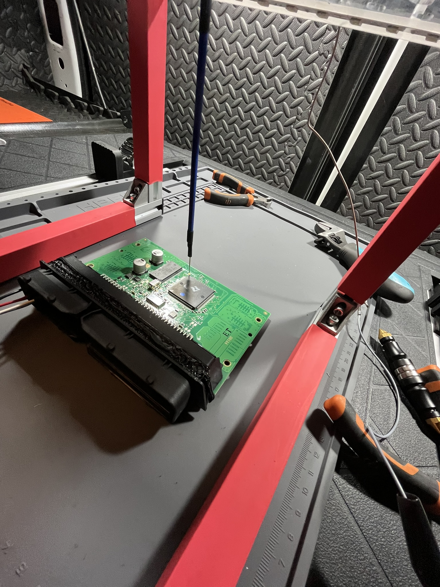 Open ECU secured in a technical frame with a probe positioned on the circuit board